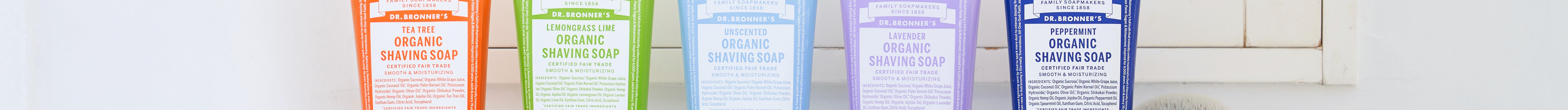 Five tubes of Dr. Bronners Organic Shaving Soap in various colors are lined up on a white tiled bathroom shelf, emphasizing a vibrant, eco friendly product display