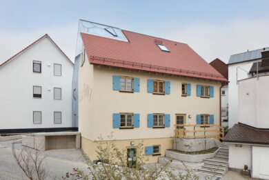 Exterior of the 3-story building with red roof and blue shutters