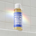 A bottle of Dr. Bronners 18 in 1 Pure Castile Magic Soap Peppermint is standing upright on a tiled shelf. A subtle rainbow reflection appears on the bottle, highlighting its eco friendly design [3.4 oz]