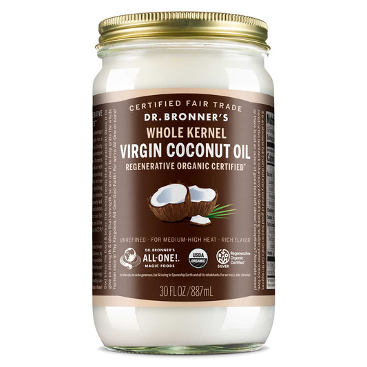 A glass jar with a gold lid contains Dr. Bronners Whole Kernel Virgin Coconut Oil. Its labeled Regenerative Organic Certified and 30 FL OZ 887 mL. The label highlights it as Certified Fair Trade and suitable for medium high heat cooking [30 oz]