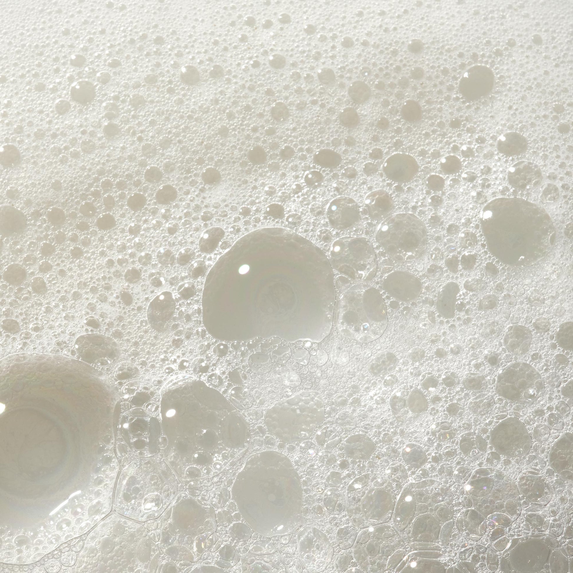 Bubbles form and float on a foamy surface, possibly indicating soap lather. The texture suggests a cleansing action in a bathroom or kitchen setting, showcasing the lightness and purity of the soap [2 oz, 3.4 oz, 4 oz, 8 oz, 16 oz, 32 oz, 1 Gallon]